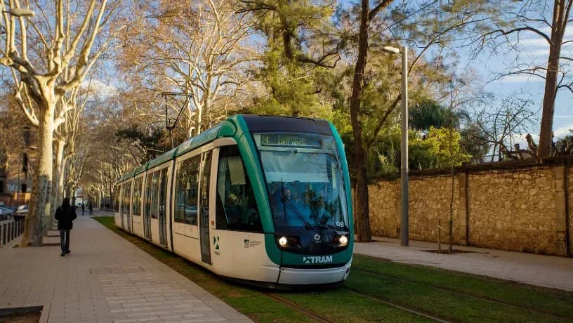 Modern TRAM vehicle traveling along a green urban street with trees and pedestrian areas.